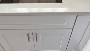 Una cocina con pileta de acero inoxidable, muebles blancos y encimera blanca.