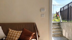 Sala de estar con un sofá marrón, un bote de basura blanco y vistas a una escalera que da al exterior.