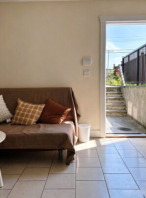 Ein Wohnzimmer mit einem braunen Sofa, einer weißen Mülltonne und Blick auf eine Treppe, die nach draußen führt.