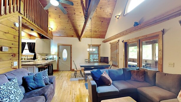 Una sala de estar acogedora con techo de madera, un comedor con mesa y sillas, y una cocina con ventana.
