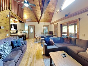 A cozy living room with a wooden ceiling, a dining area with a table and chairs, and a kitchen with a window. - Smokey Bear Haven (Pigeon Forge)
