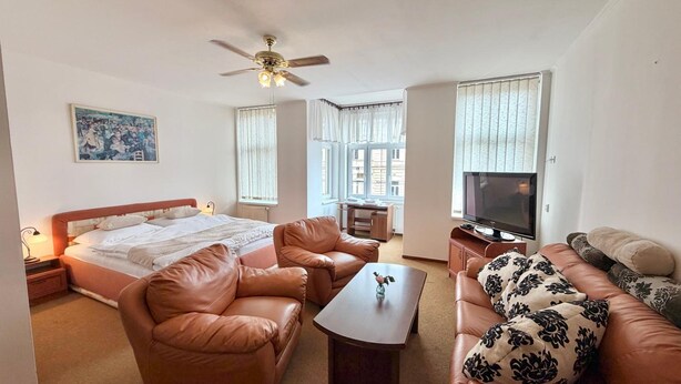 A room with a bed, two leather sofas, a coffee table, a TV, and a ceiling fan. - Hotel Zlatvo K Ov (Teplice)