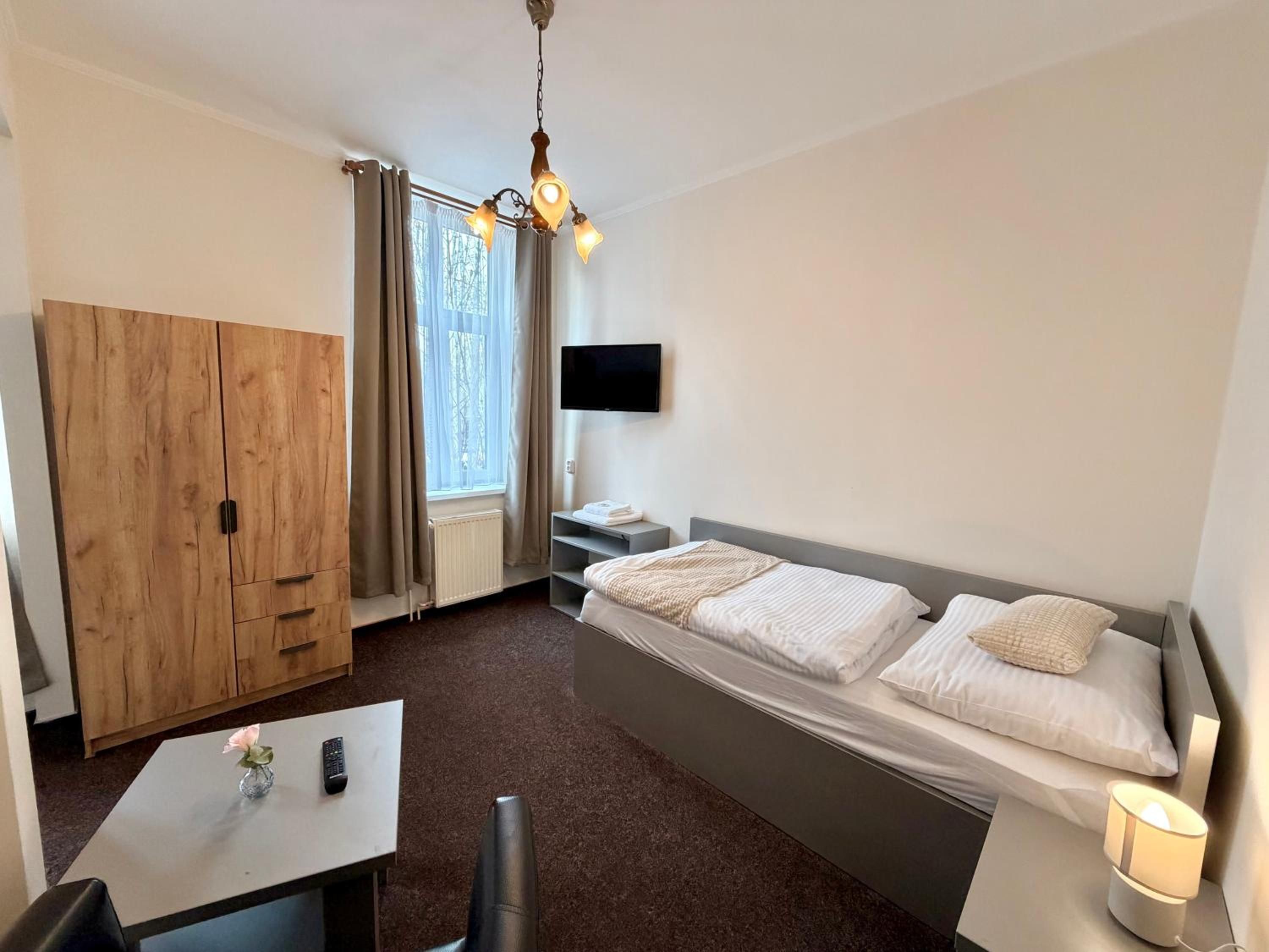 Ein Hotelzimmer mit einem Bett, einem Fernseher, einem Holzschrank, einem Schreibtisch mit einer Vase und einer Lampe.