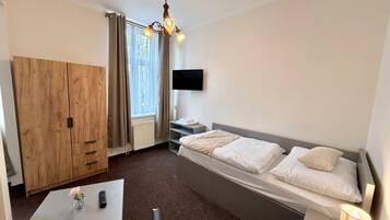 Ein Hotelzimmer mit einem Bett, einem Fernseher, einem Holzschrank, einem Schreibtisch mit einer Vase und einer Lampe.
