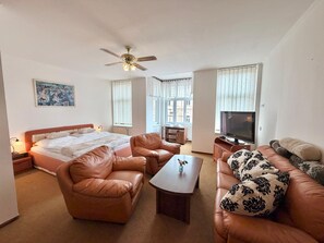 A room with a bed, two leather sofas, a coffee table, a TV, and a ceiling fan. - Hotel Zlatvo K Ov (Teplice)
