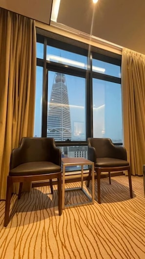 A hotel room with two leather chairs, a small table, and a large window offering a view of a tall building. - Rio Hotel (Riyadh)