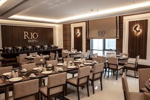 A dining area with multiple tables set for service, a bar area with a selection of beverages, and the hotel's name displayed on the walls. - Rio Hotel (Riyadh)