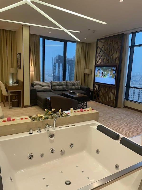 A modern hotel room with a large bathtub, a sofa, a TV, and a city view. - Rio Hotel (Riyadh)