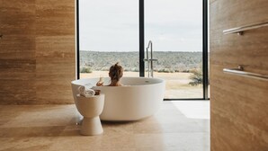 Ein modernes Badezimmer mit einer großen Badewanne, einer Toilette und Blick auf eine Wüstenlandschaft durch große Fenster.