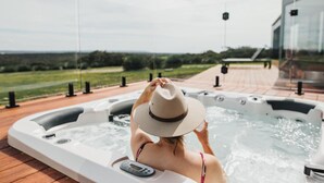 Eine Person entspannt sich in einer Hot Tub mit Blick auf eine Landschaft und ein Gebäude im Hintergrund.
