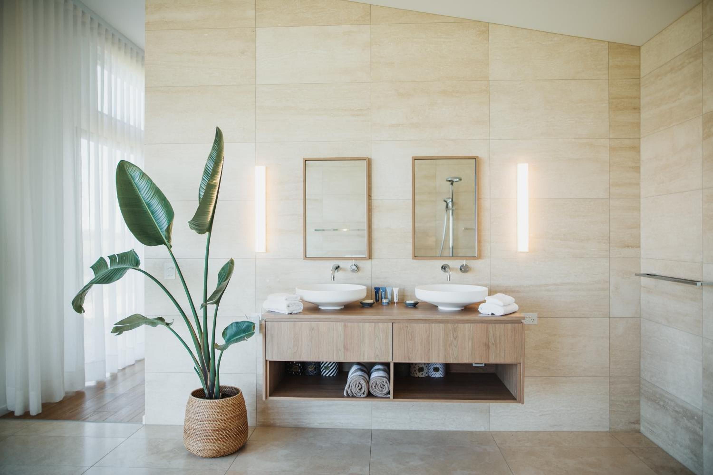 A modern bathroom with two sinks, a large mirror, and a potted plant.