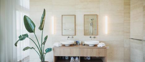 A modern bathroom with two sinks, a large mirror, and a potted plant.