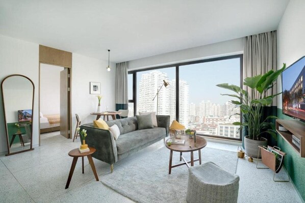 A modern living room with a grey sofa, a coffee table, a TV, and a large window with a city view. - Baseplus-binjiang Serviced Apartment (Shanghai)