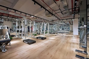 Un gimnasio con diversos equipos de ejercicio, suelo de madera y pared espejada.