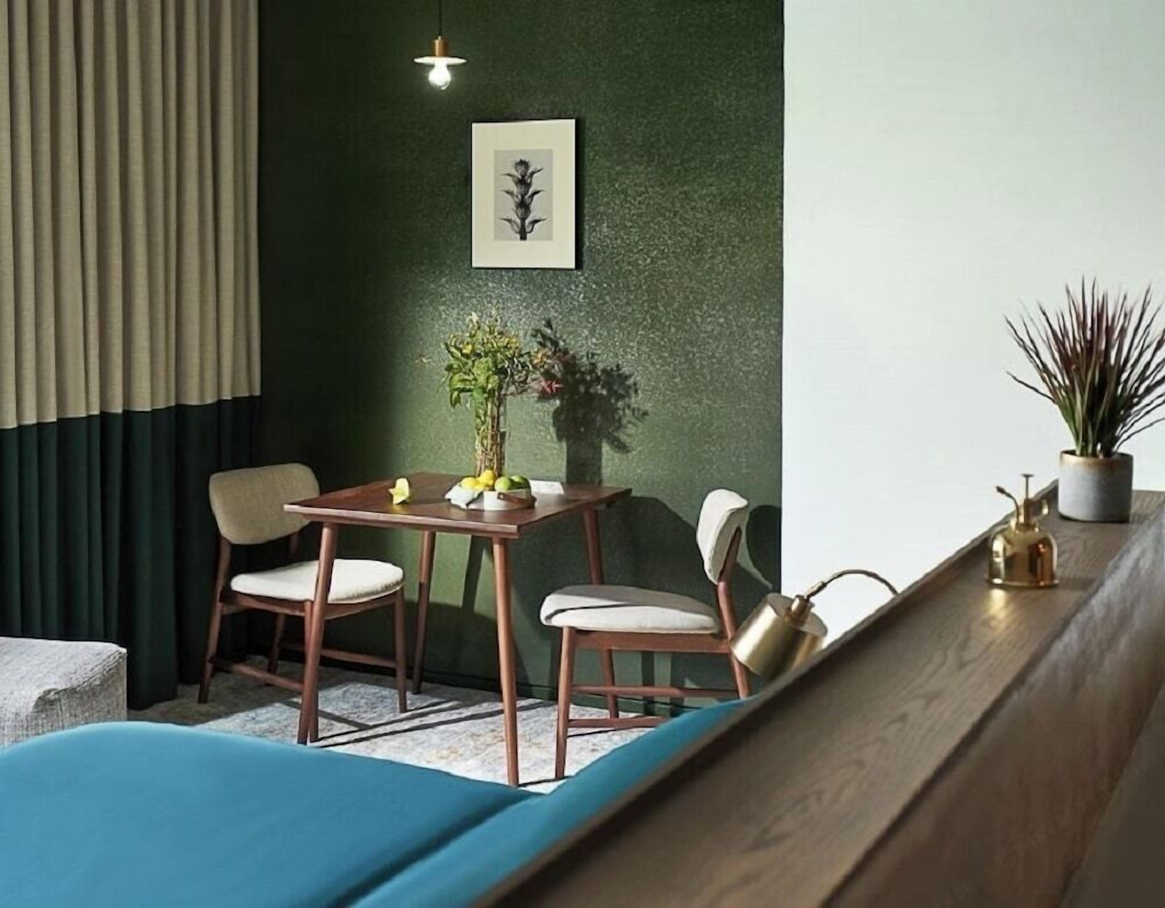 A room with a green wall, a wooden table with chairs, a potted plant, and a small table lamp.