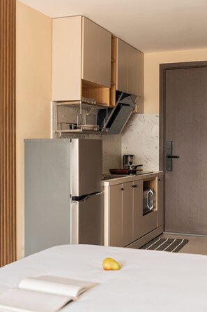 Eine kompakte Küche mit Kühlschrank, Ofen und Mikrowelle, einem Holzkasten und einer Tür zum Schlafzimmer.