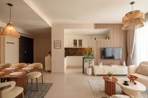 Un salon moderne avec un coin repas, une cuisine à l’arrière-plan, un téléviseur à écran plat et une grande fenêtre avec des rideaux.