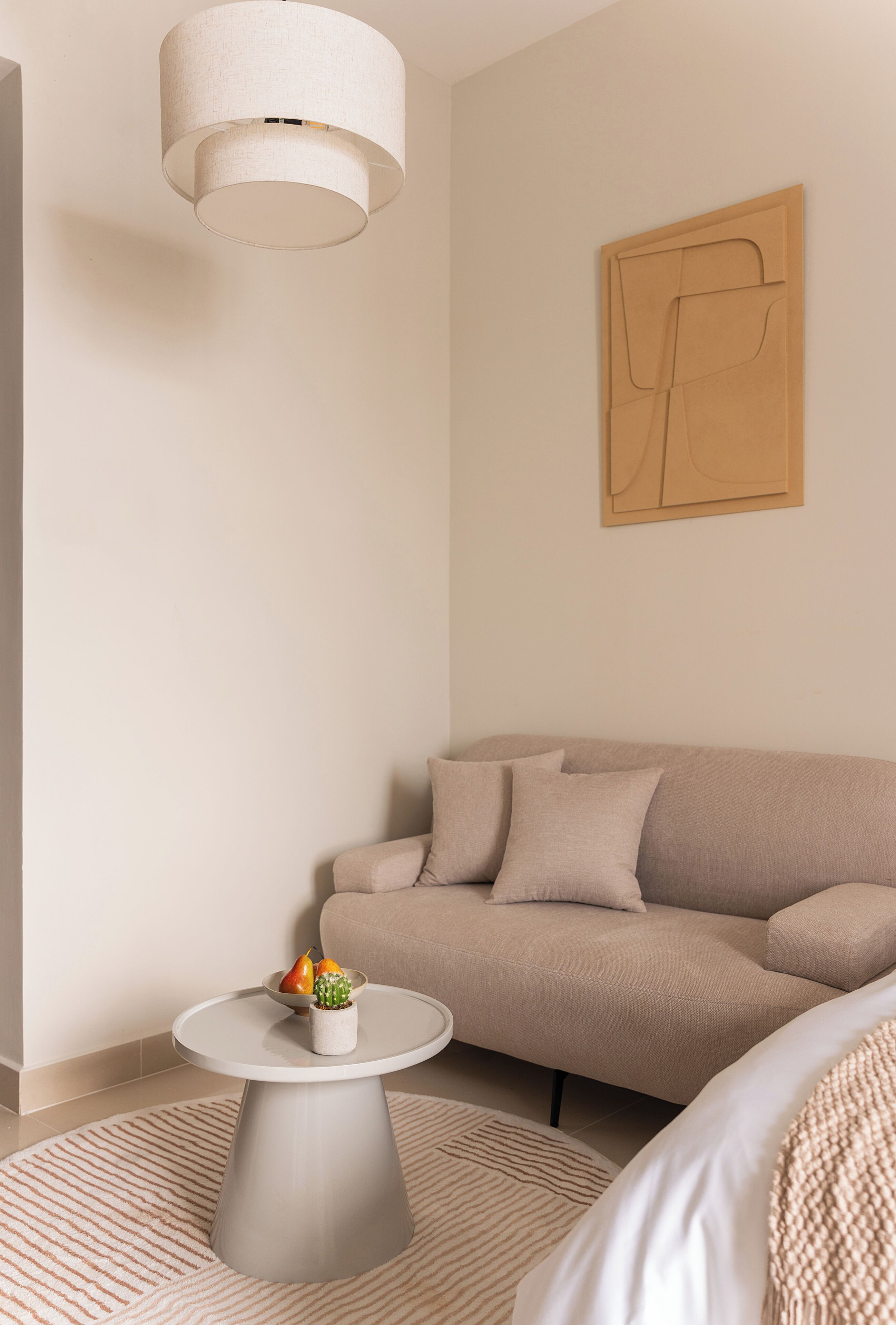 En minimalistisk stue med sofa, lille sofabord, hængende lampe og et kunstværk på væggen.