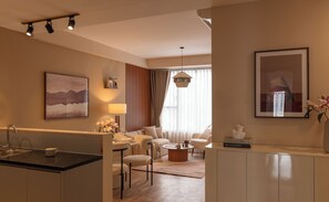 Ein modernes Hotelzimmer mit Küchenbereich, einem Wohnzimmer mit Sofa und Sesseln, einem Esstisch und einem großen Fenster mit Vorhängen.