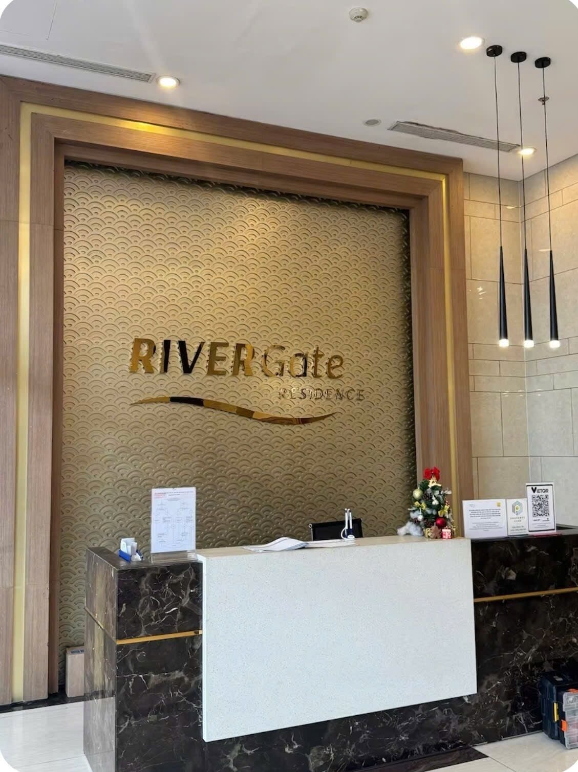 A reception desk with a marble counter, a decorative wall with the text 'RIVERGate RESIDENCE', and a small Christmas tree.