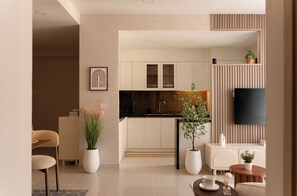 A modern living room with a dining area, a kitchen with white cabinets, a flat-screen TV mounted on a wall, and a potted plant. - Maison De Gu Rivergate (Ho Chi Minh City)