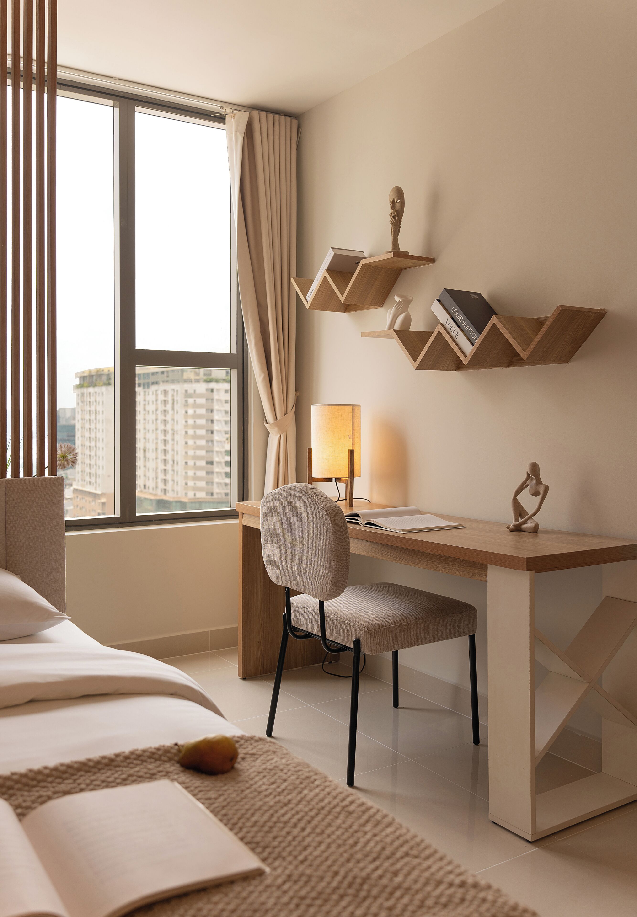 Habitación de hotel con cama, escritorio, silla, lámpara y vista a la ciudad por la ventana.