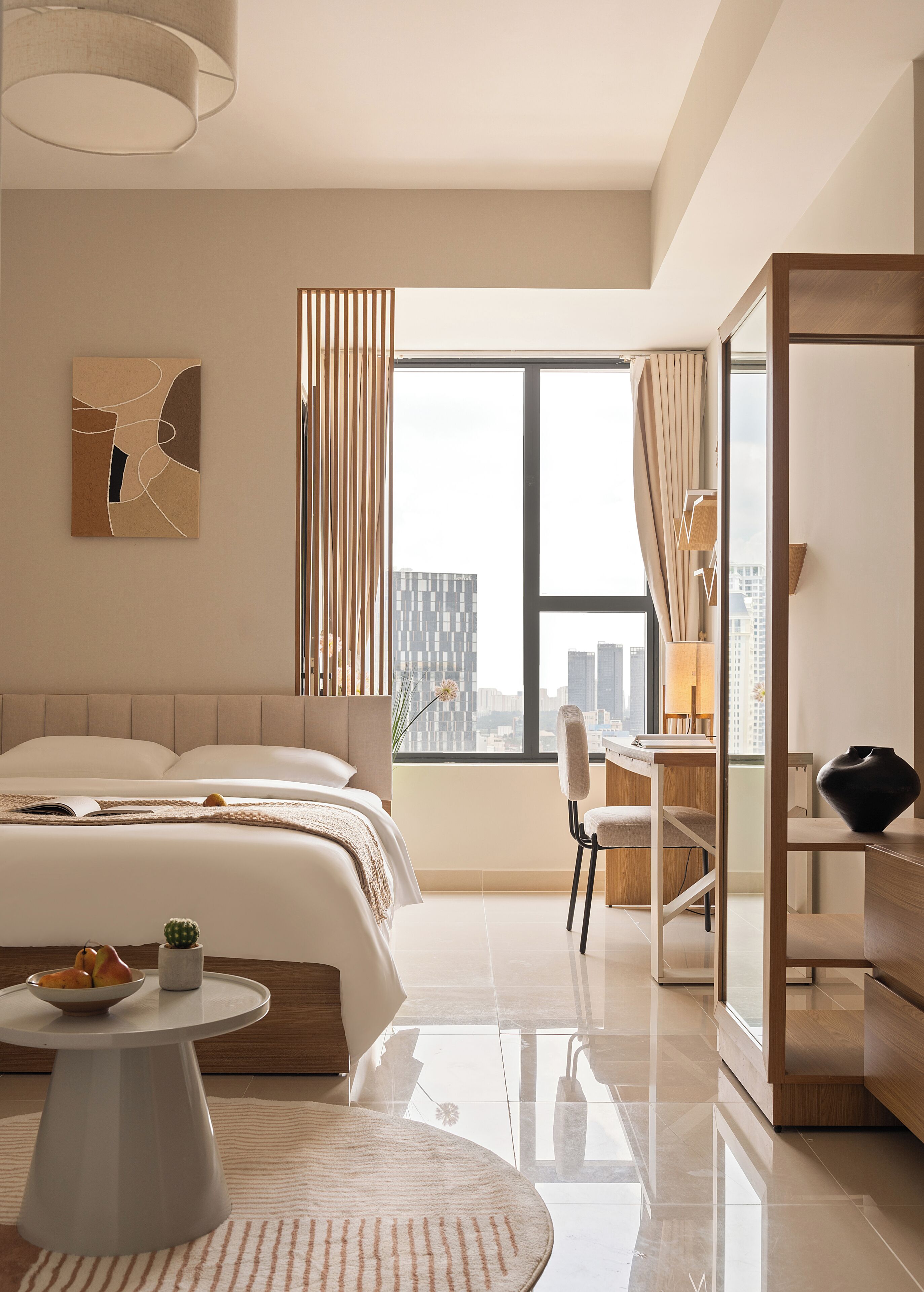 A modern hotel room with a large bed, a desk, a chair, a round coffee table, and a view of the city through a large window.