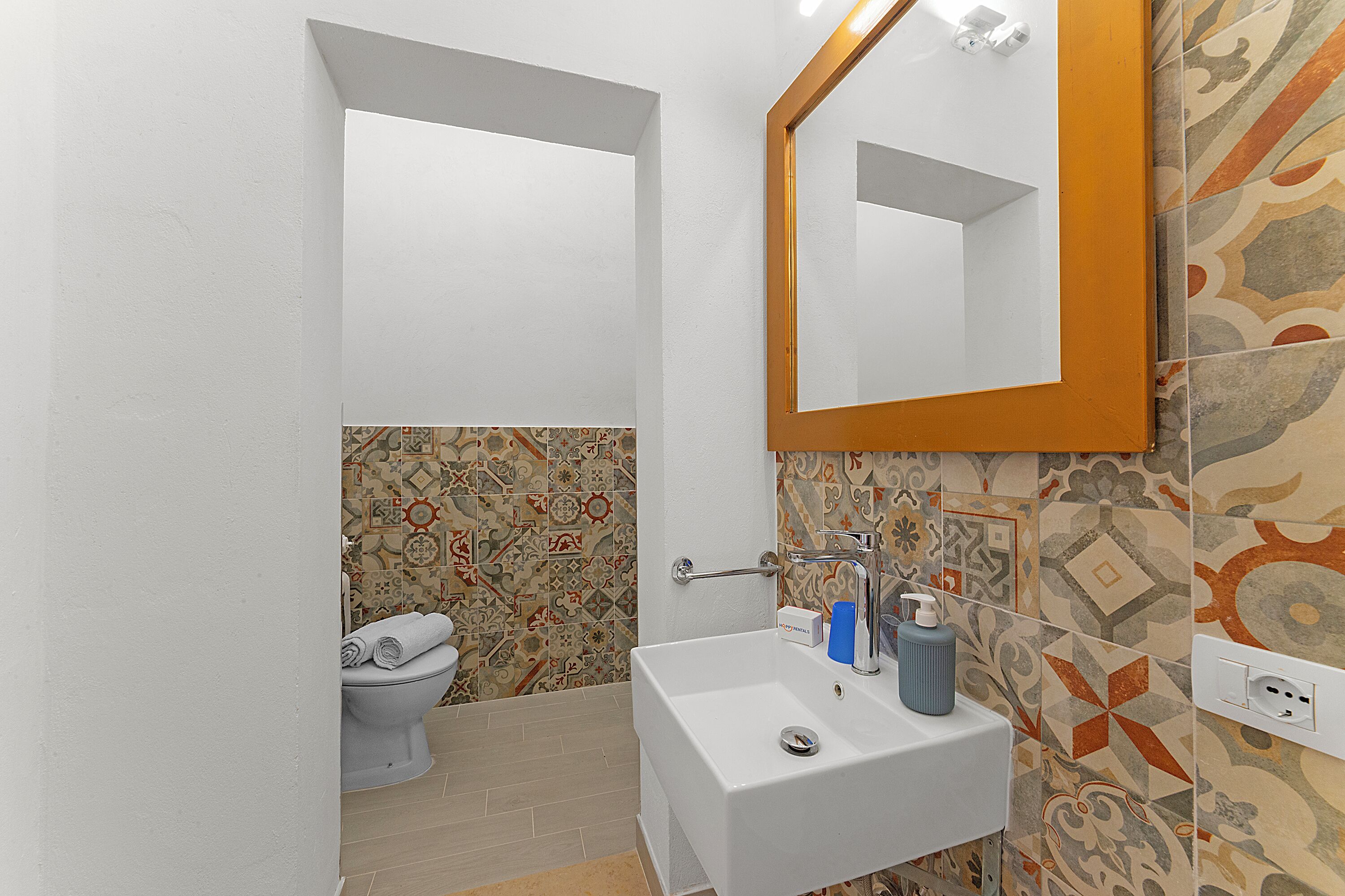 A bathroom with a white sink, a mirror, and patterned tiles.