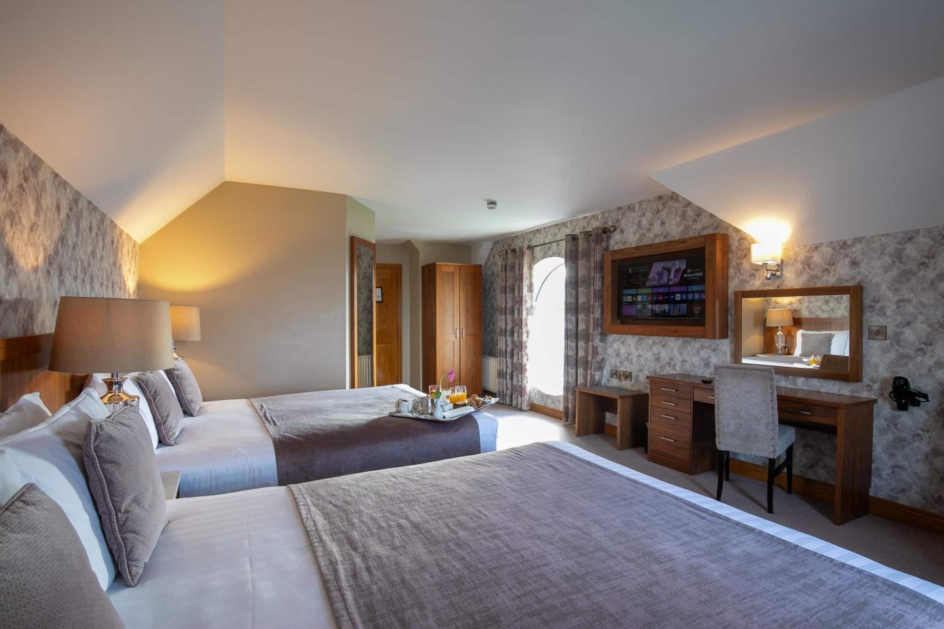 Habitación de hotel con dos camas, un escritorio, una silla, un televisor y un baño visible a través de una puerta abierta.