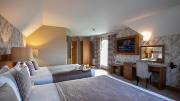 Habitación de hotel con dos camas, un escritorio, una silla, un televisor y un baño visible a través de una puerta abierta.