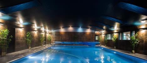 A swimming pool with a tiled floor and walls, surrounded by potted plants and recessed lighting.