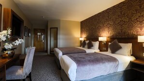 A hotel room with two beds, a desk, a chair, and a patterned wallpaper. - The Holyrood Hotel (Bundoran)