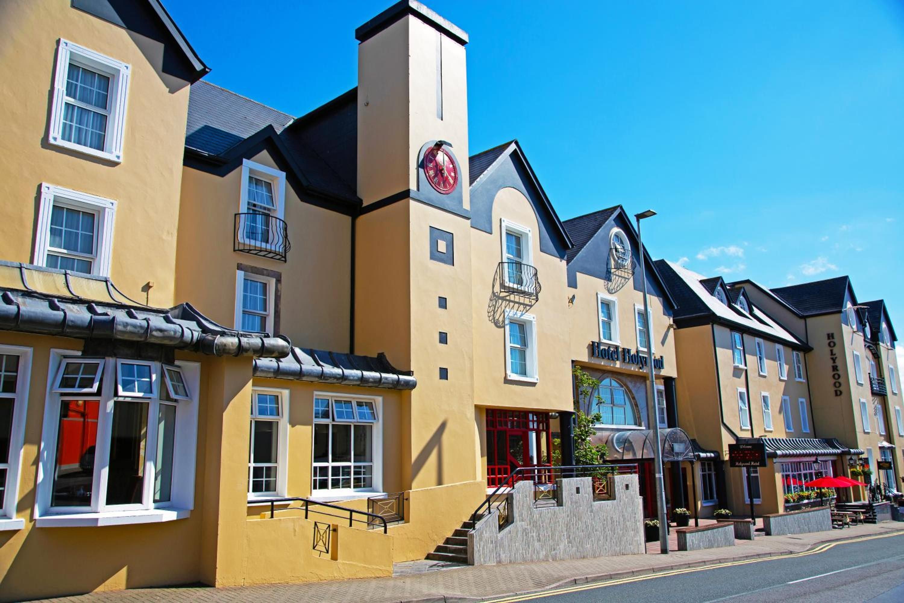 A row of yellow buildings with multiple windows and balconies, a clock, and a sign that reads 'Hotel Bury.'