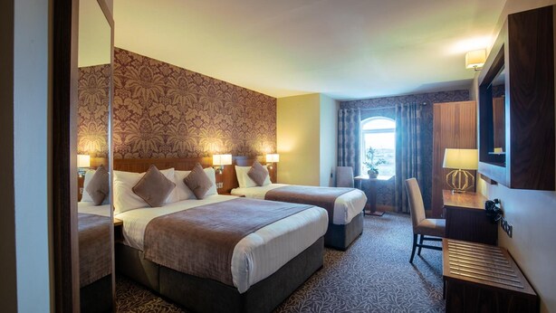 A hotel room with two beds, a desk, a chair, and a large mirror. - The Holyrood Hotel (Bundoran)