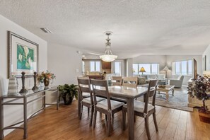 A spacious living area with a dining table, chairs, a sofa, and a kitchen in the background. - Gorgeous 5th Floor Oceanfront Views | Pet Friendly | Super Spacious 1 Bedroom (Fernandina Beach)