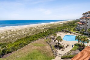 Un complexe hôtelier doté d’une piscine, offrant une vue sur la plage et comprenant un bâtiment avec de nombreux balcons.