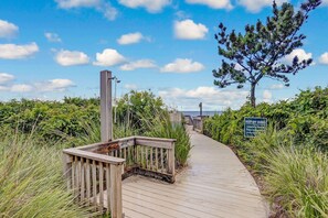 Une promenade en bois mène à une zone de plage où un panneau indique qu’il est interdit de marcher sur les dunes.