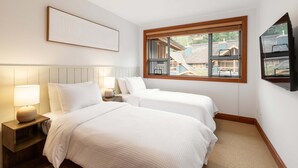 A bedroom with two beds, a nightstand, a lamp, a window with a view of buildings, and a framed picture on the wall. - Modern 3BR | Walk to Whistler Village | Hot Tub | AC | Pet-Friendly (Whistler)