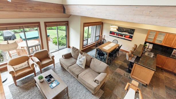 A spacious living area with a sofa, coffee table, and dining table, connected to a kitchen with a bar and a dining area. - Modern 3BR | Walk to Whistler Village | Hot Tub | AC | Pet-Friendly (Whistler)