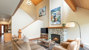 A spacious living room with a stone fireplace, a staircase, and a television. - Modern 3BR | Walk to Whistler Village | Hot Tub | AC | Pet-Friendly (Whistler)