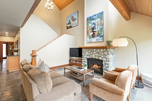 A spacious living room with a stone fireplace, a staircase, and a television. - Modern 3BR | Walk to Whistler Village | Hot Tub | AC | Pet-Friendly (Whistler)