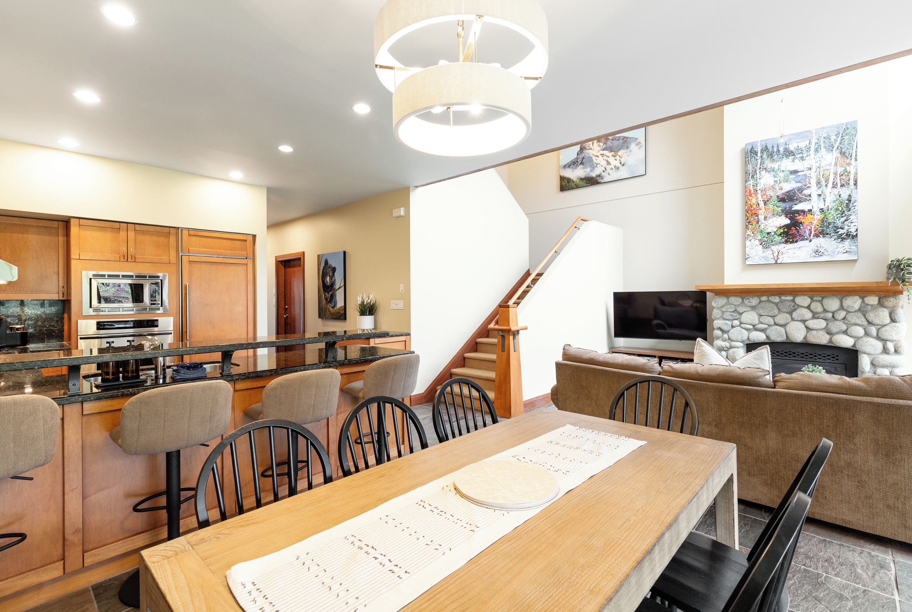 A modern kitchen with a dining area, a staircase, and a living room with a fireplace.