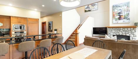 A modern kitchen with a dining area, a staircase, and a living room with a fireplace.