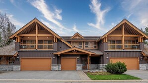 A modern multi-story house with a central entrance, large garage doors, and a stone foundation. - Modern 3BR | Walk to Whistler Village | Hot Tub | AC | Pet-Friendly (Whistler)