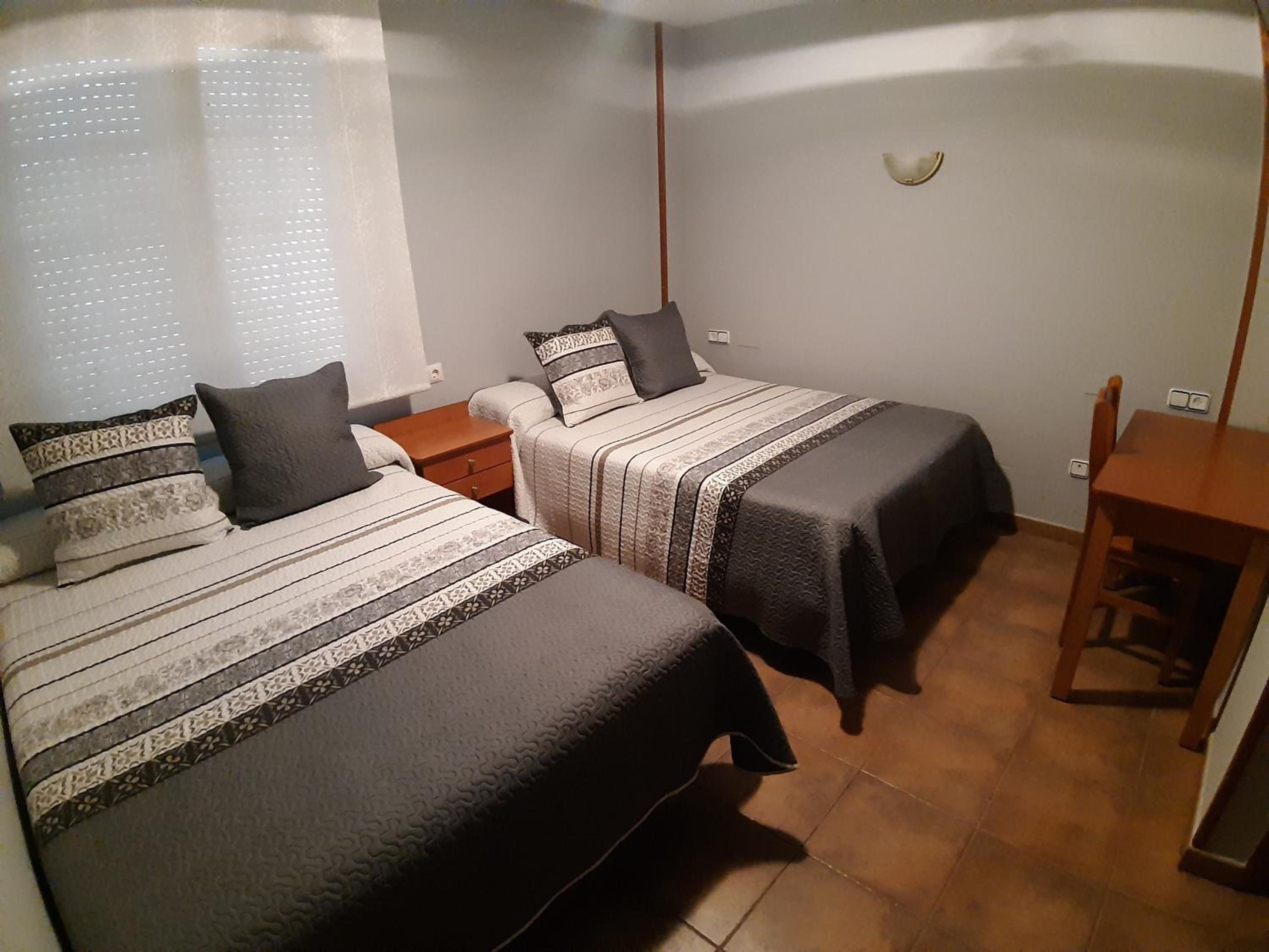 A bedroom with two beds, a nightstand, a chair, and a small table.