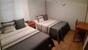 Un dormitorio con dos camas, una mesita de noche, una silla y una pequeña mesa.