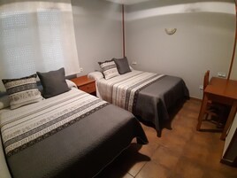 Un dormitorio con dos camas, una mesita de noche, una silla y una pequeña mesa.