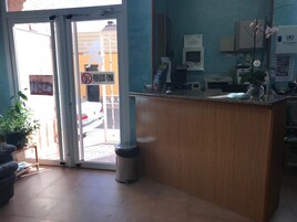 Zona de recepción con escritorio, un bote de basura, una planta en maceta y un cartel que prohíbe fumar.