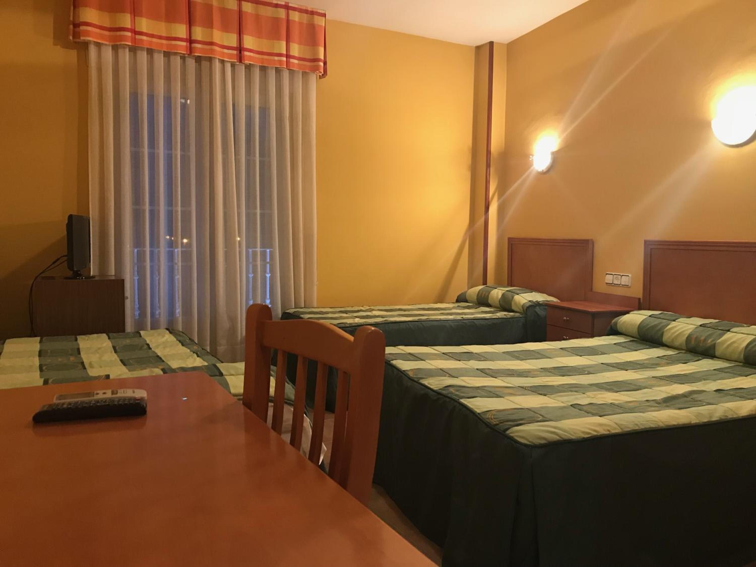 A hotel room with two beds, a wooden table, a TV on a stand, and a window with curtains.