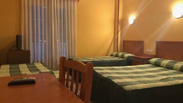 A hotel room with two beds, a wooden table, a TV on a stand, and a window with curtains.